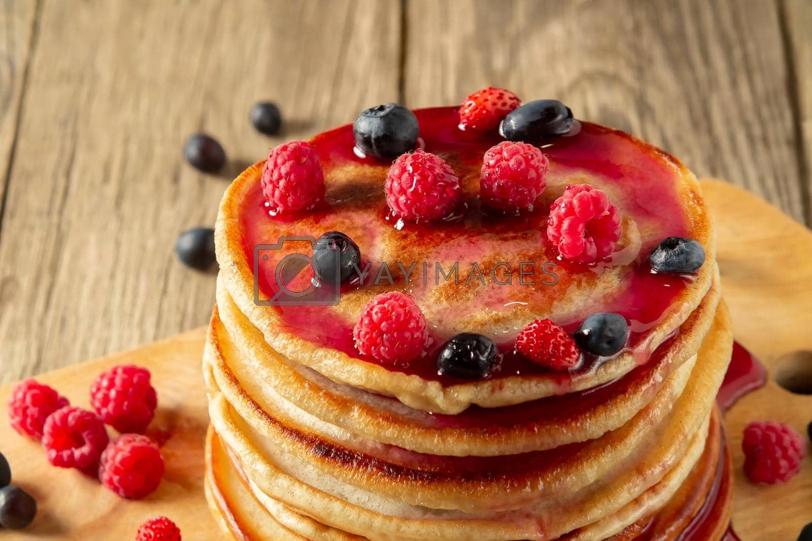Royalty free image of Stack of pancakes with syrup and fresh berries on wooden board on table by galsand