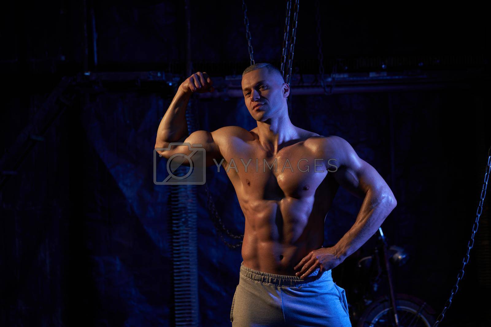 Royalty free image of Young shirtless muscular man standing among metal chains, looking at camera, copy space by andreonegin