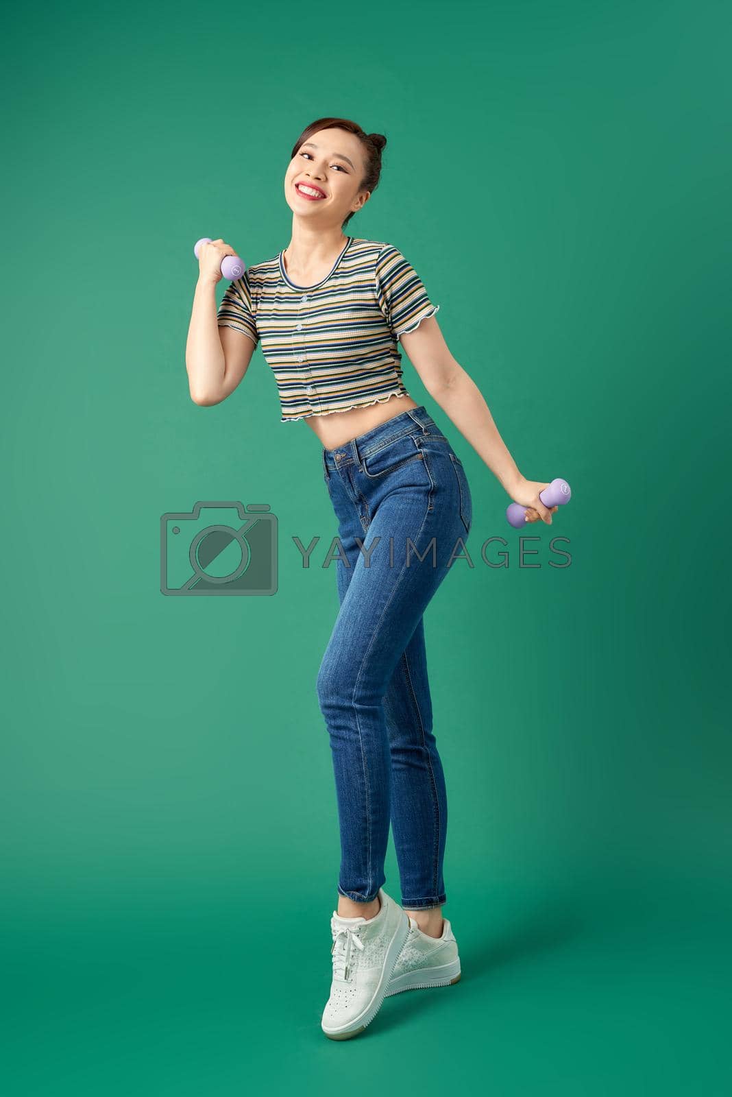 Royalty free image of Attractive young Asian woman holding dumbell while standing over green background. Full length. by makidotvn