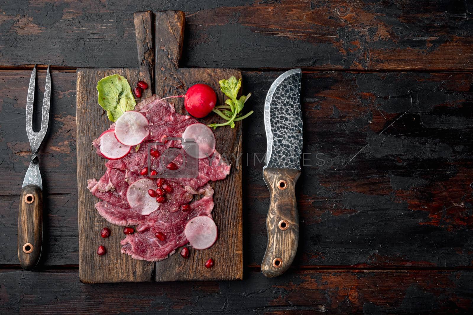 Royalty free image of Beef Carpaccio cold appetizer, with Radish and garnet, on wooden serving board, on old dark wooden table background, top view flat lay, with copy space for text by Ilianesolenyi