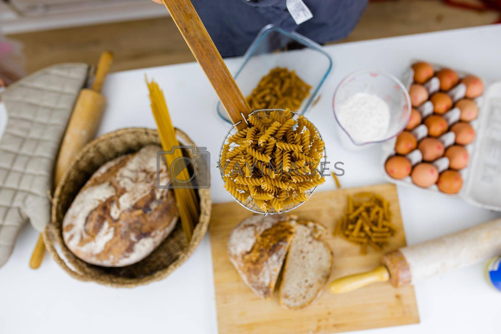 Royalty free image of Uncooked fusilli on wooden pasta strainer above ingredients on a table by Kanelbulle