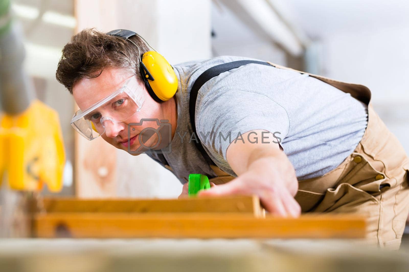 Royalty free image of Carpenter using electric saw in carpentry by Kzenon