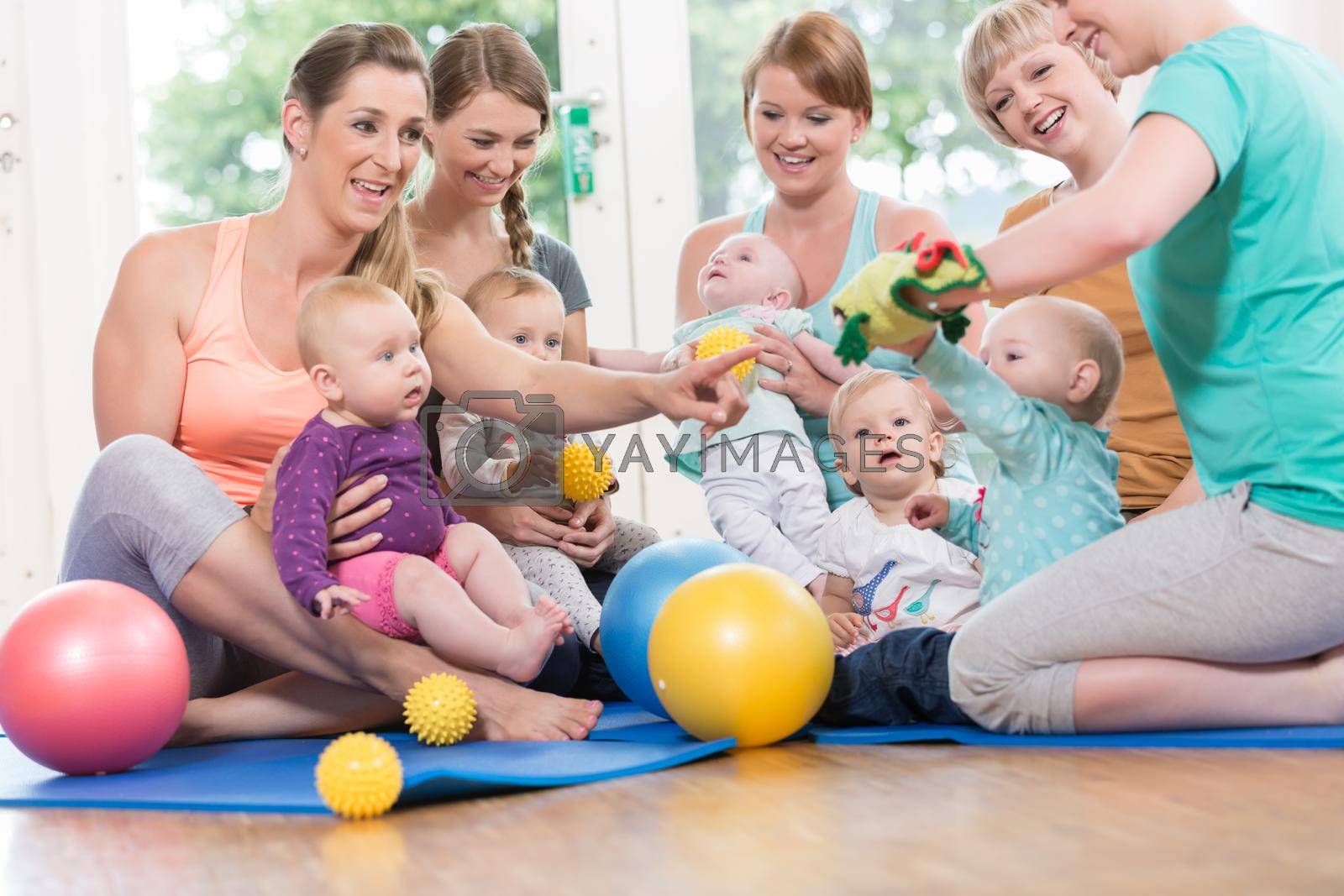 Royalty free image of Young women in mother and child group playing with their babies by Kzenon