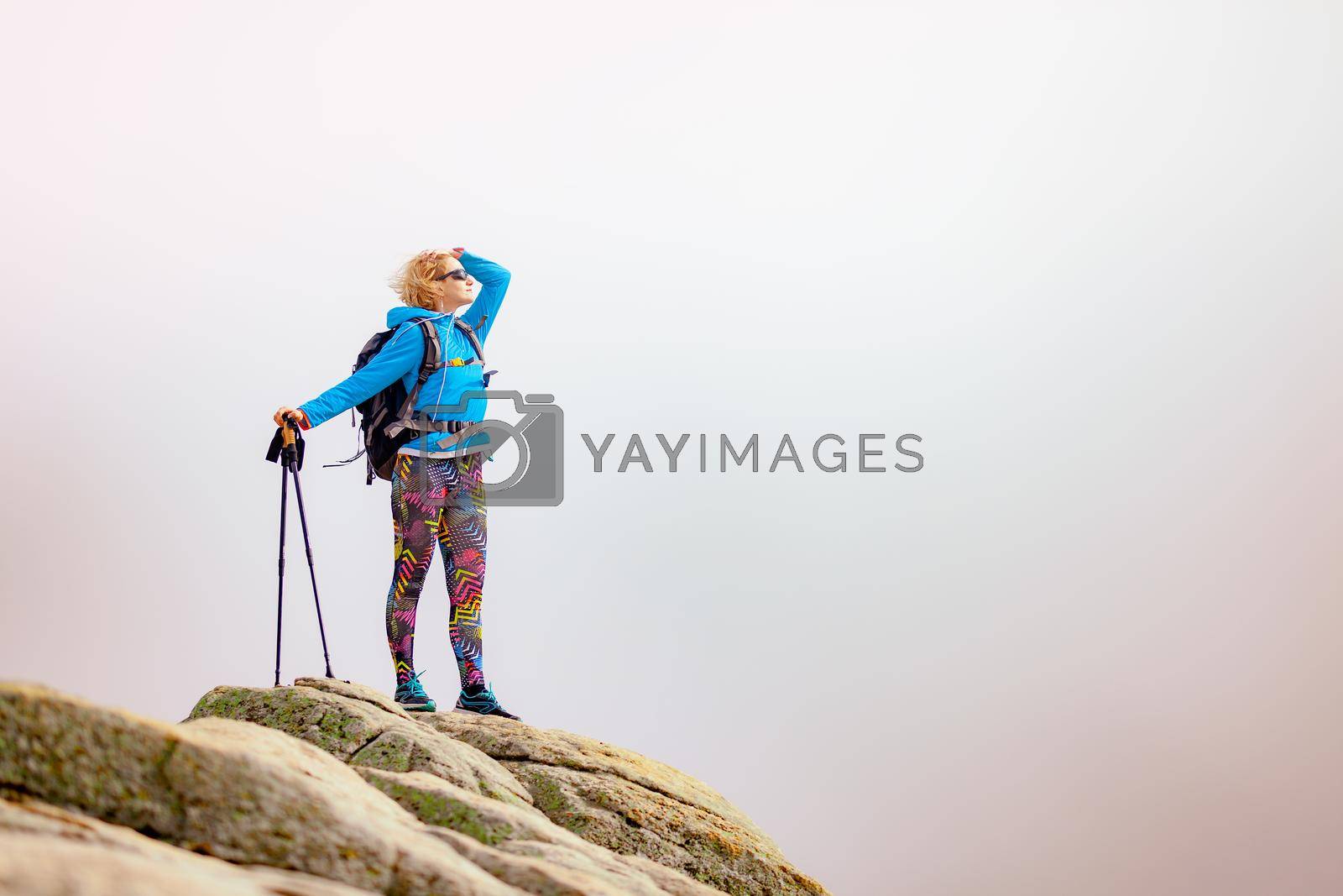 Royalty free image of Hiking girl with poles and backpack standing on rocks. Windy autumn day. Travel and healthy lifestyle outdoors in fall season by kokimk