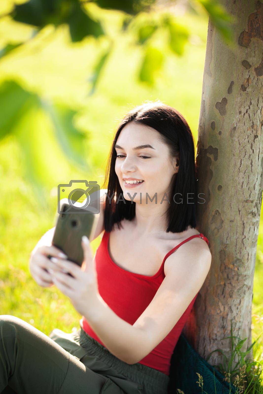 Royalty free image of happy dark brown hair girl with her smartphone under a tree by kokimk
