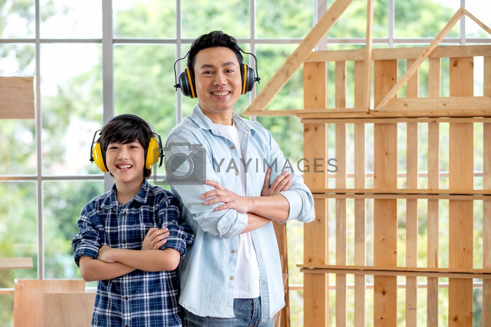 Royalty free image of Portrait of Asian father and boy with mechanic headphone stand in front of woodwork and look at camera. by nrradmin