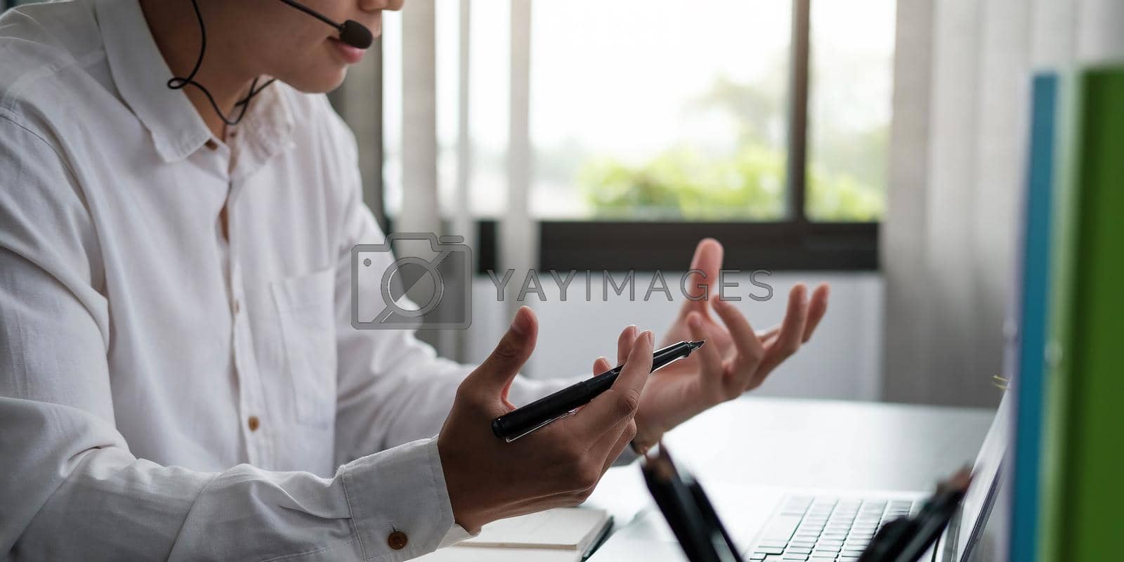 Royalty free image of Young man teacher coach wearing headphones speaking, holding online lesson. Focused student looking at computer monitor screen by wichayada