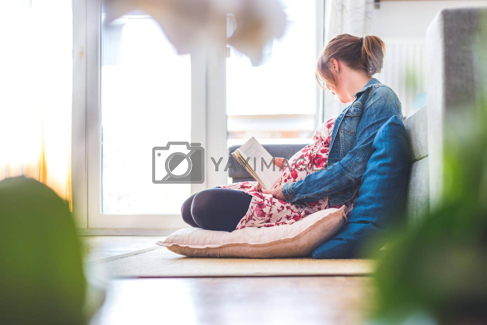 Pregnant caucasian happy mother is sitting on the floor, reading a book
