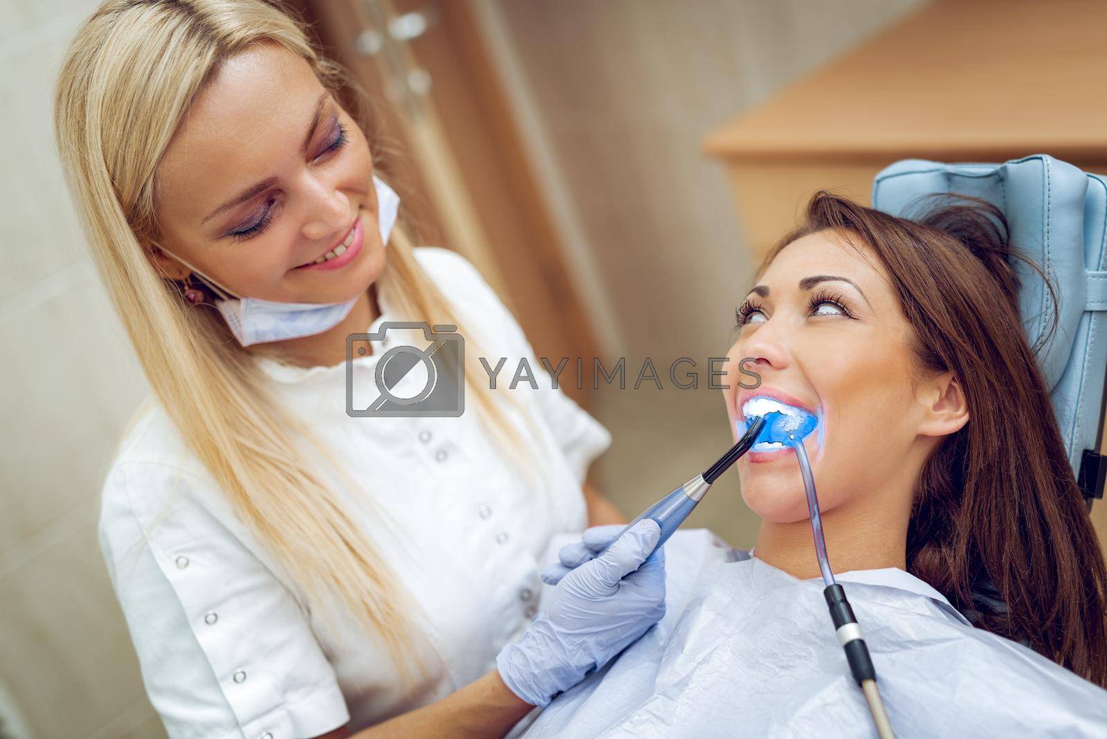 Beautiful young smiling woman at visit in the dentist office and dentist finishing repair tooth with dental curing UV lamp. 