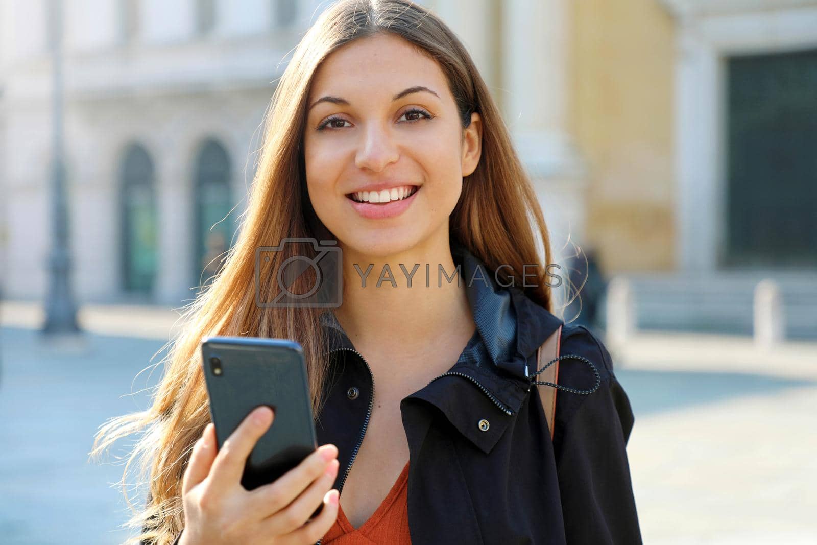 Royalty free image of Brazilian bright cheerful student girl holding smart phone and looks at camera by sergio_monti