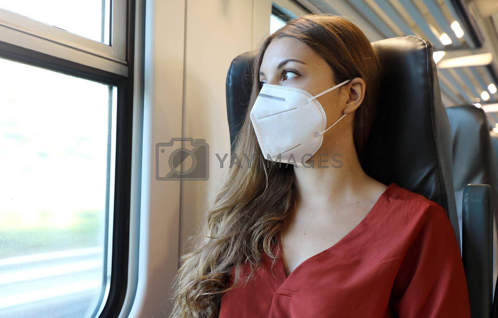Travel safely on public transport. Young woman with face mask looking through train window. Train passenger with protective mask traveling early morning to go to work.