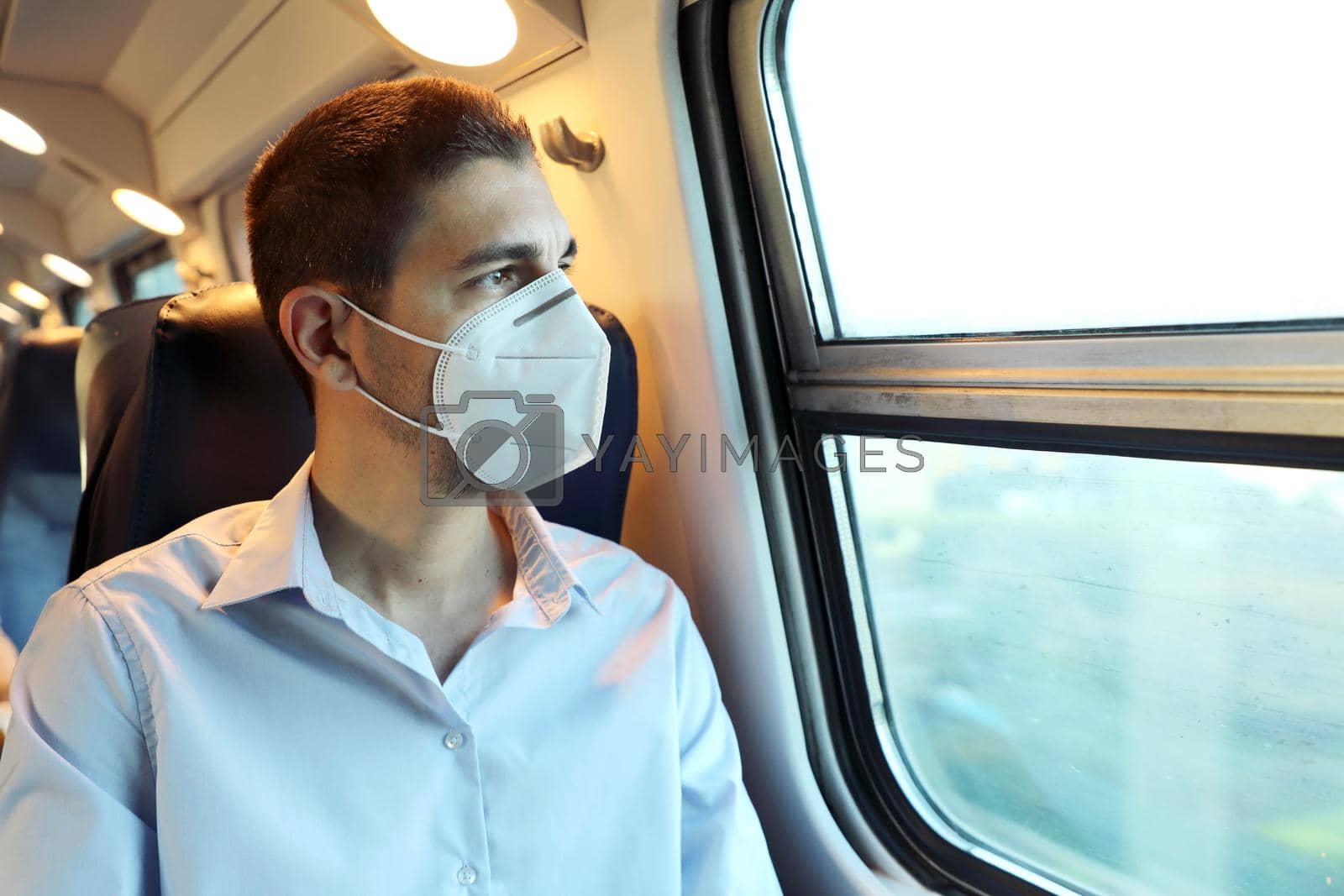 Travel safely on public transport. Young man with KN95 FFP2 face mask looking through train window. Train passenger with protective mask looking through the window.
