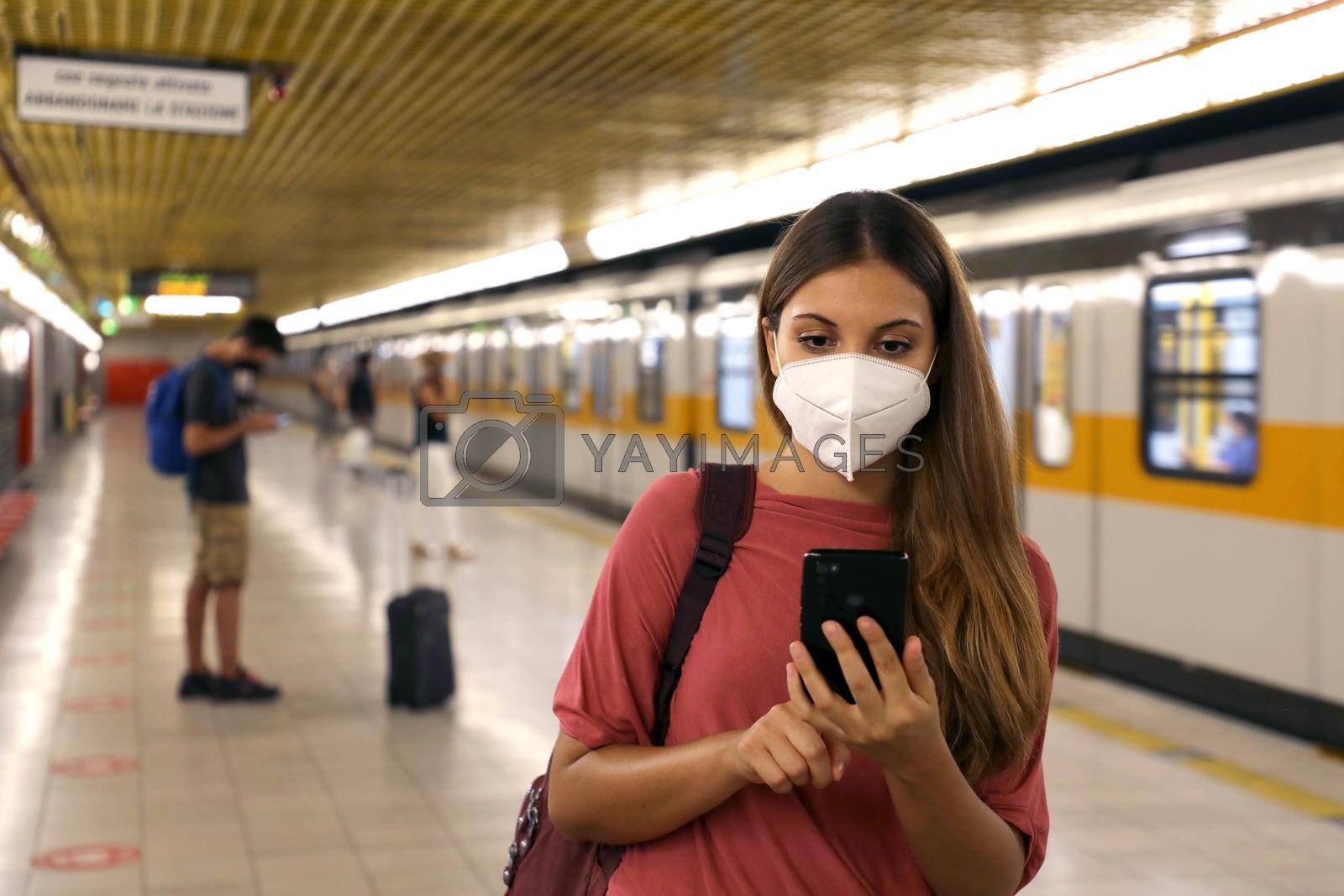 Portrait of young woman with protective mask using smart phone app in the subway train station