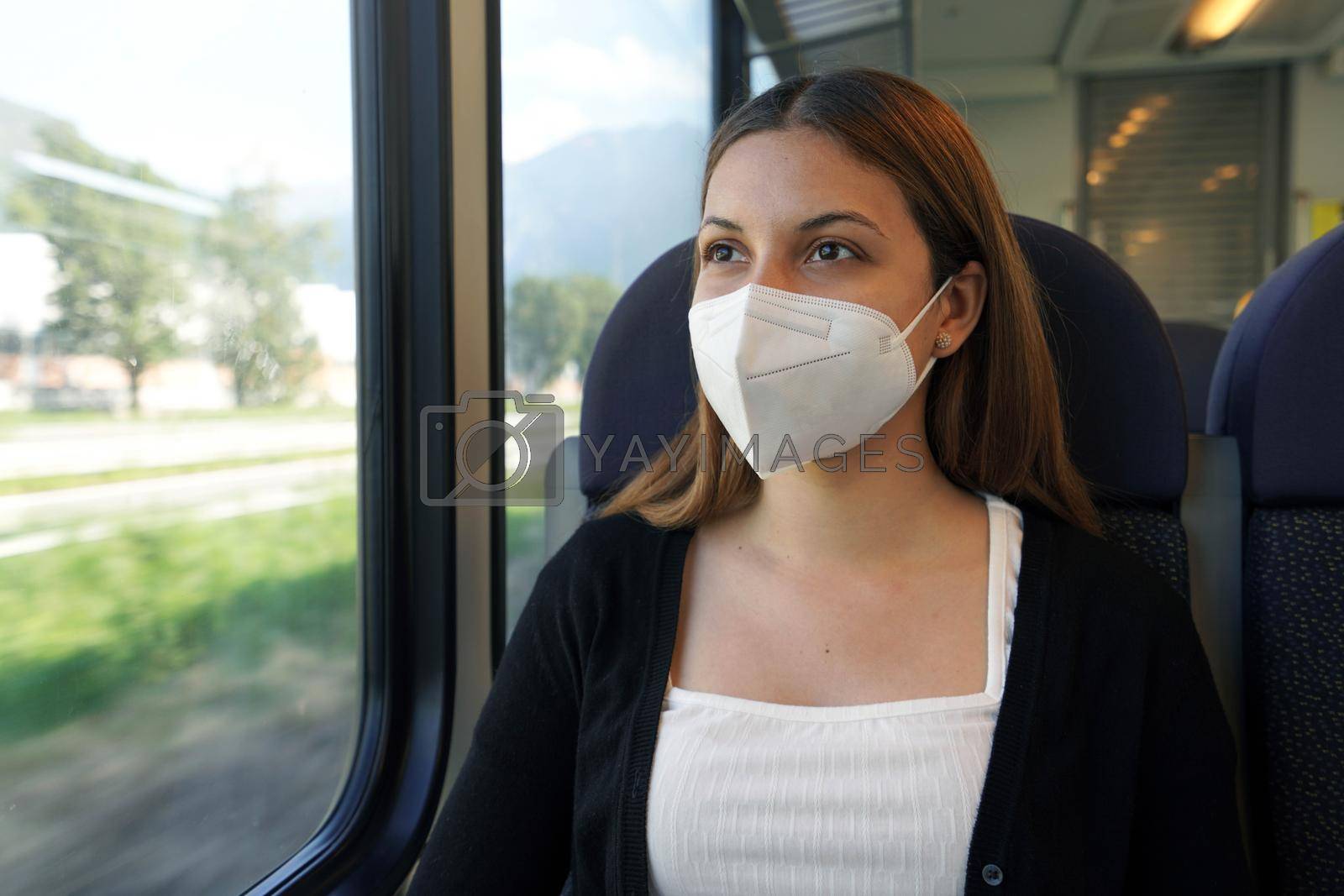 Travel safely on public transport. Young woman with KN95 FFP2 face mask looking through train window. Train passenger with protective mask.