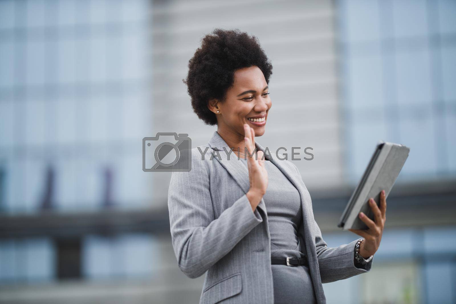 Portrait of a smiling black business woman making video call on a digital tablet in front a corporate building.