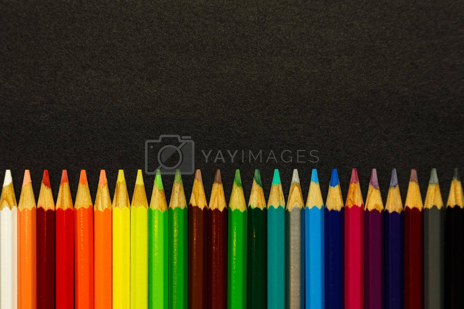 Royalty free image of A bunch of colorful pencils lined up over a dark background by AveCalvar