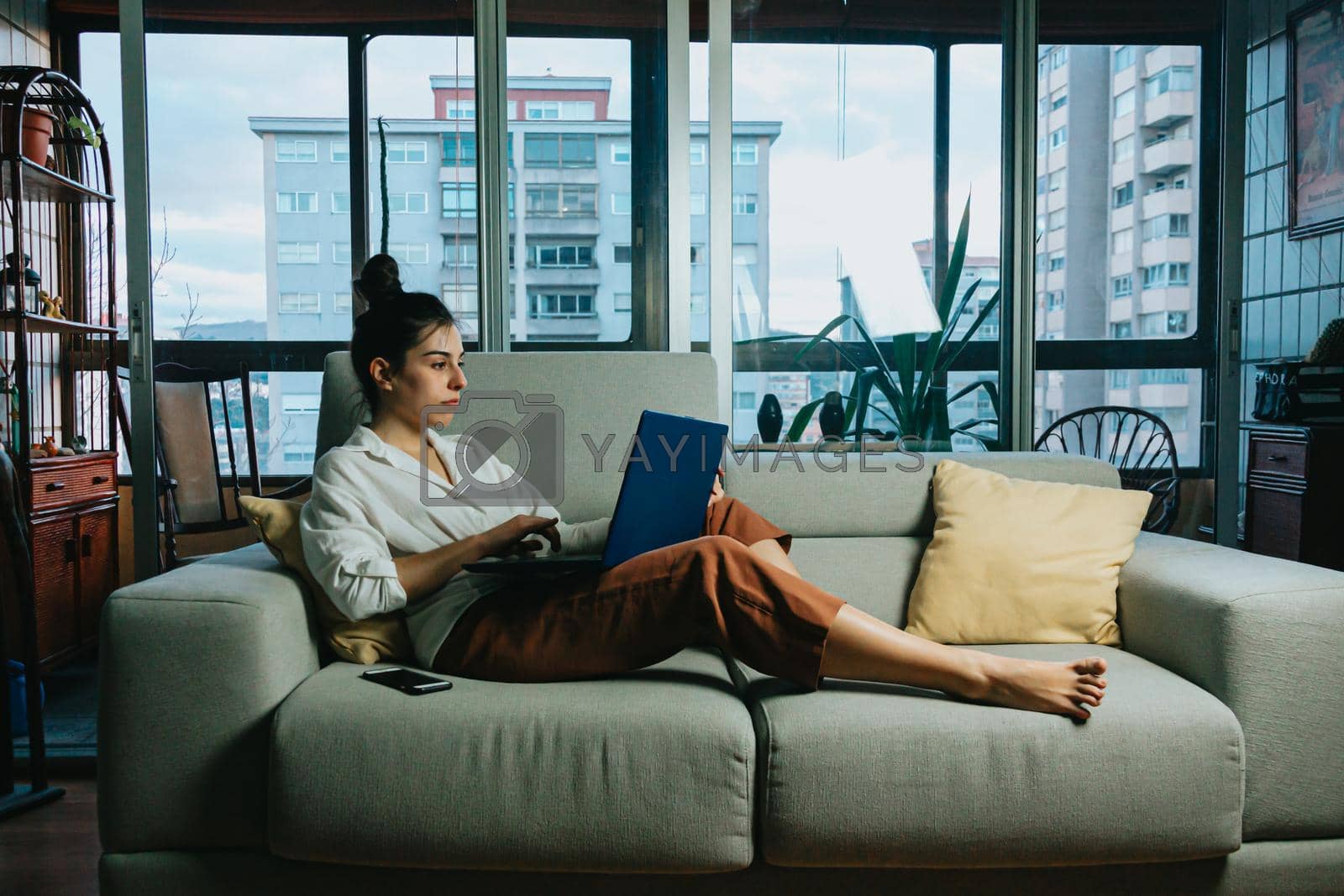 Royalty free image of A young woman working on his laptop from home during the pandemic in the city on a modern flat by AveCalvar