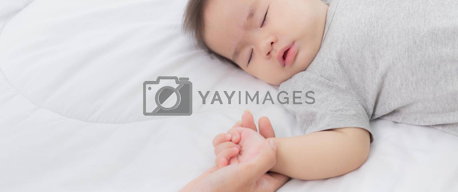Royalty free image of Young asian mother touch hand of little baby girl with tender on bed in the bedroom, mom love newborn and care, woman with expression with child together, parent and daughter, family concept. by nnudoo