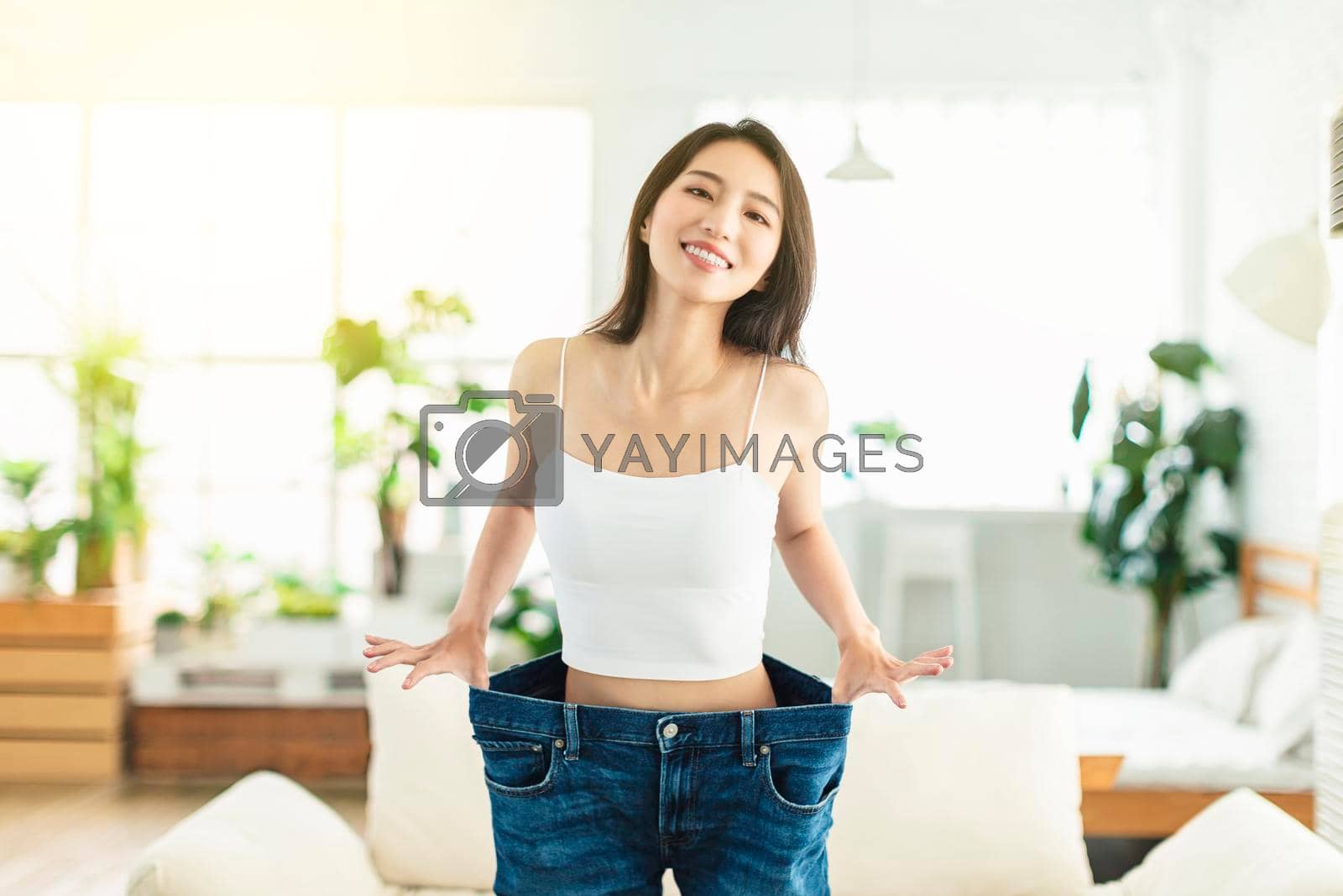 Royalty free image of A young woman, wearing big-size jeans before losing weight, and pulling it back and forth, is very happy that she has succeeded in losing weight and is very satisfied with her current figure by tomwang