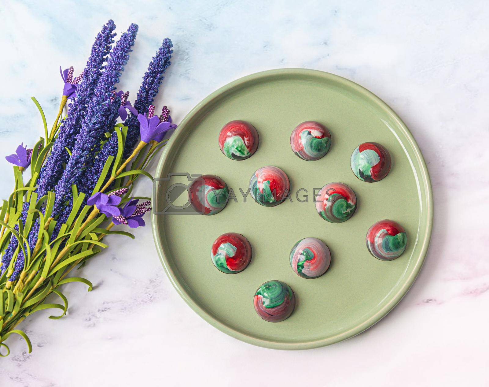 Royalty free image of Collectible handmade tempered chocolate sweets with a glossy painted body on a round plate with blur elements. View from above by Grommik