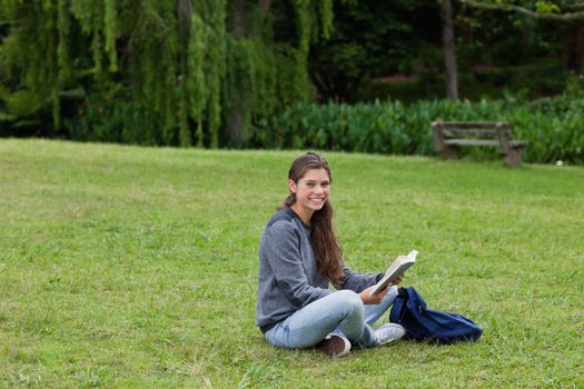 Smiling young adult reading a book while sitting cross-legged