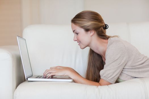 Side view of young woman lying on the sofa with her laptop