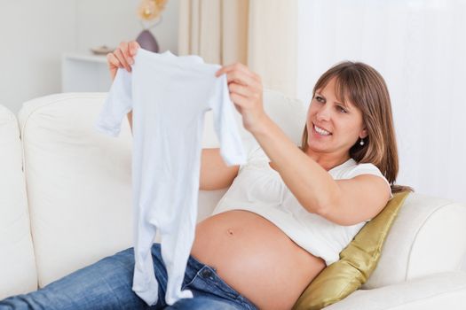 Pretty pregnant woman holding a baby grow while lying on a sofa