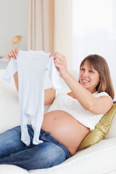 Lovely pregnant woman holding a baby grow while lying on a sofa