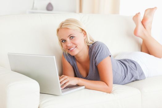 Lying blonde woman using a laptop in her living room