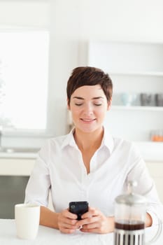A woman sitting with her mobile phone and a coffee in the kitchen