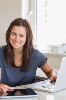 Smiling brunette using the tablet pc and laptop