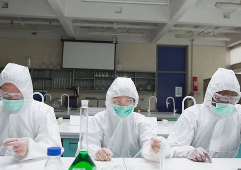 Chemists in protective suits adding liquid to petri dishes
