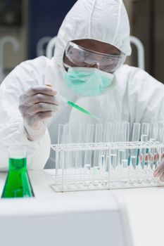 Chemist adding green liquid to test  tubes