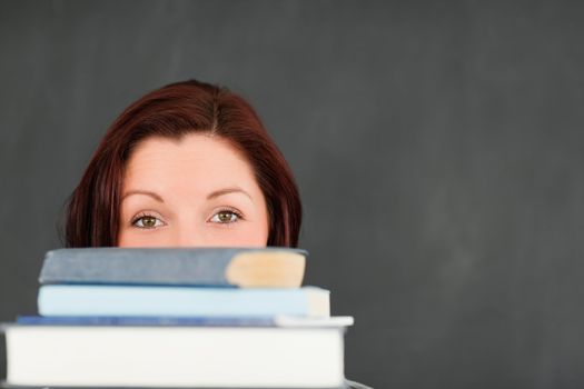 Close up of a young woman hidding behind a stack of books