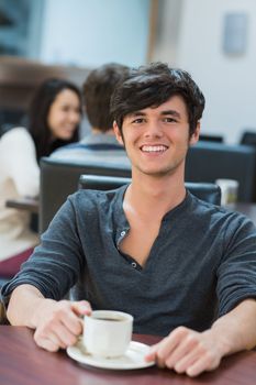 Man sitting at table drinking coffee while smiling in college cafe
