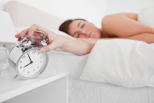 Charming brunette female awaking with a clock while lying