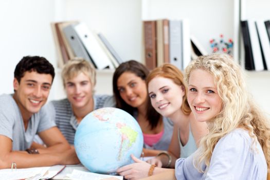 Smiling teenagers in a library working with a terrestrial globe