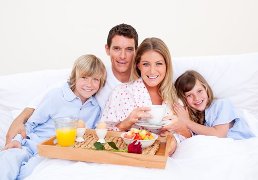 Smiling family having breakfast sitting on bed