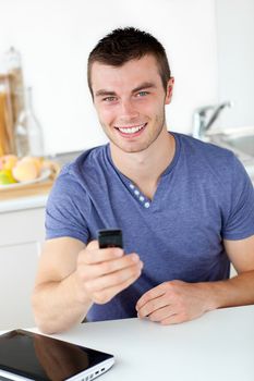 Lively young man sending a text smiling at the camera