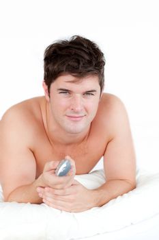 Handsome man lying on his bed and holding a remote against a white background