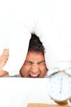 Man stressed by his alarm clock putting his head under the pillow in the bedroom 