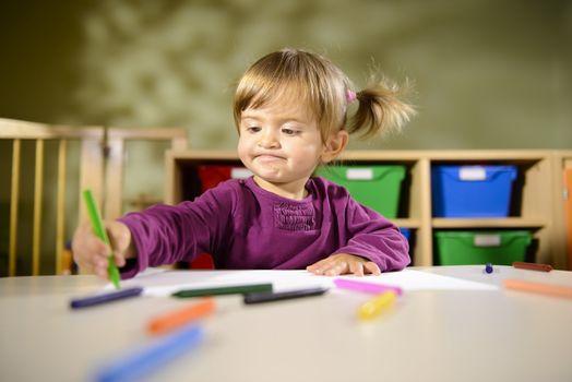 Little girl having fun at school and drawing with colors in kindergarten