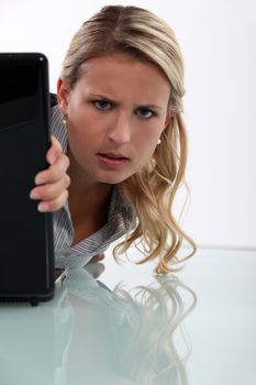 Annoyed woman peeking round her laptop