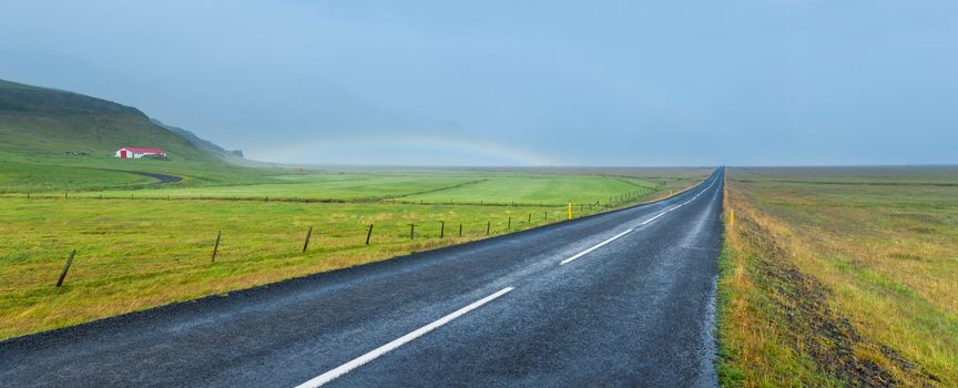 Iceland - famous Ring Road (Hringvegur). Rainbow over asphalt highway. Panorama
