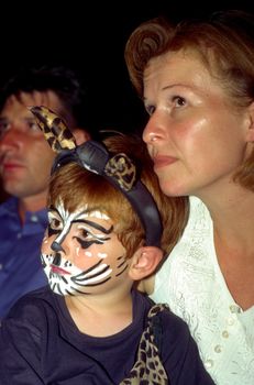 boy and mother are watching a performance, boy has a cat makeup 