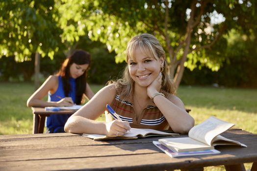 People and education, two young women studying with book for university test in park and smiling at camera