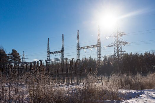 Sun on the electric power transmission lines near road in the winter against the blue sky with fog