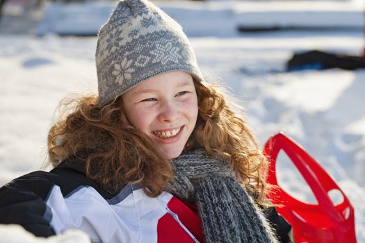 Relaxed girl in winter cloths with red sledge
