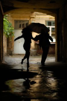silhouette of couple with umbrella running from rain