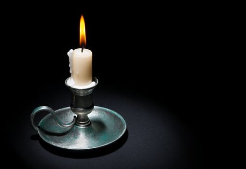 Lighted candle in an old tin candlestick on a black  background